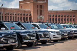 luxury vehicles parked outside Kenya parliament. Each car has a small flag at the front.